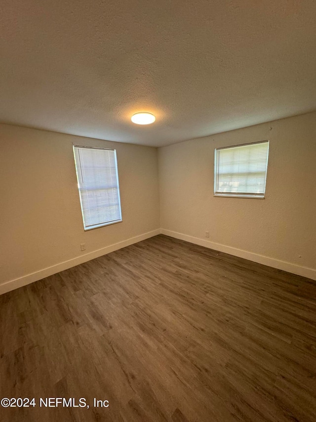 empty room with a textured ceiling, dark hardwood / wood-style floors, and a healthy amount of sunlight