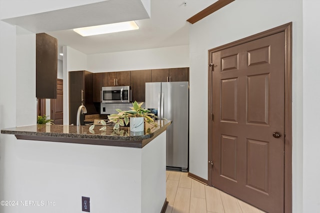 kitchen with kitchen peninsula, appliances with stainless steel finishes, dark brown cabinets, sink, and dark stone countertops