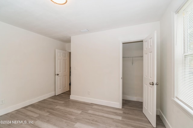 unfurnished bedroom with multiple windows, a closet, and light wood-type flooring