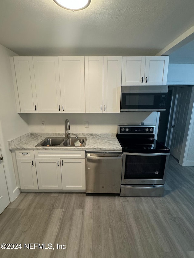 kitchen featuring stainless steel appliances, white cabinetry, light hardwood / wood-style floors, and sink