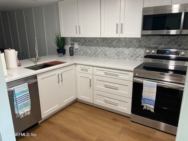 kitchen with sink, tasteful backsplash, appliances with stainless steel finishes, white cabinets, and light wood-type flooring