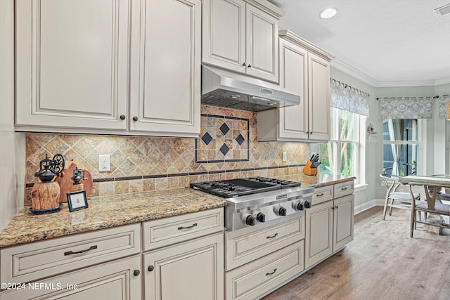 kitchen with light wood-type flooring, light stone countertops, stainless steel gas stovetop, ornamental molding, and backsplash