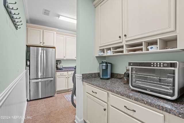 kitchen with stainless steel fridge, cream cabinetry, dark stone countertops, light tile patterned floors, and a textured ceiling