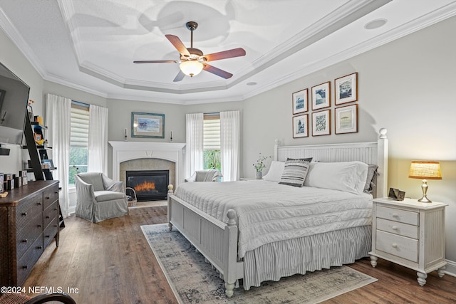 bedroom with a tile fireplace, ceiling fan, crown molding, dark wood-type flooring, and a raised ceiling