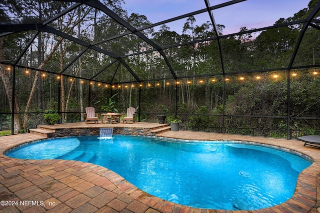 pool at dusk with glass enclosure, pool water feature, and a patio area