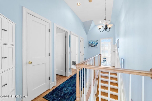 hallway featuring light hardwood / wood-style flooring, lofted ceiling, and an inviting chandelier