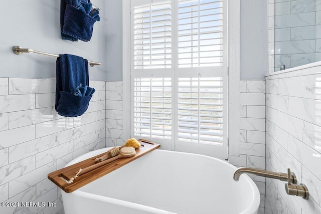 bathroom with a tub, a wealth of natural light, and tile walls