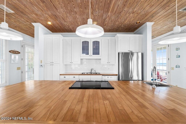 kitchen with white cabinetry, stainless steel refrigerator, hanging light fixtures, and sink