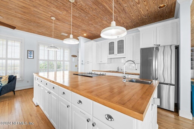 kitchen with stainless steel fridge, light wood-type flooring, a kitchen island with sink, butcher block countertops, and white cabinetry