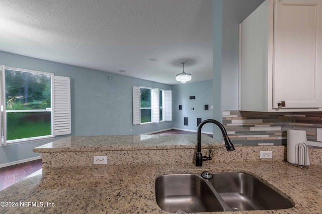 kitchen with hardwood / wood-style floors, light stone counters, a textured ceiling, sink, and white cabinetry