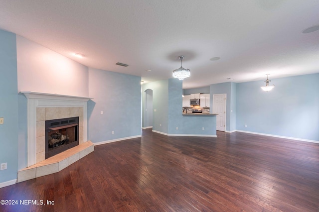 unfurnished living room featuring a tiled fireplace and dark hardwood / wood-style floors