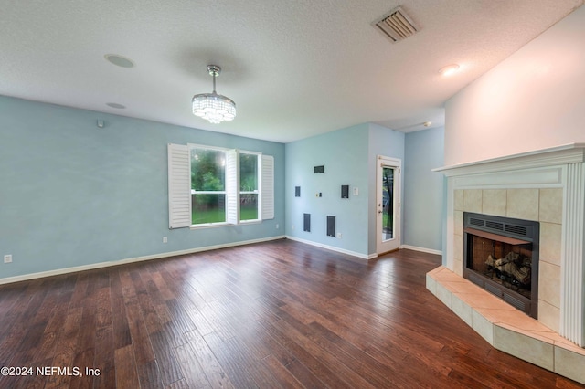 unfurnished living room featuring an inviting chandelier, dark hardwood / wood-style flooring, a textured ceiling, and a tiled fireplace