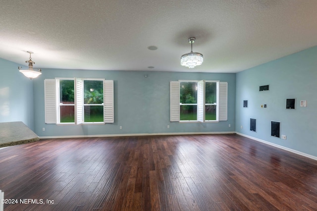 spare room featuring a notable chandelier, dark hardwood / wood-style flooring, a textured ceiling, and a healthy amount of sunlight