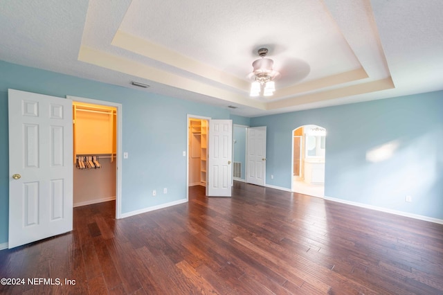 unfurnished bedroom featuring ceiling fan, dark hardwood / wood-style flooring, and a walk in closet