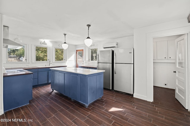 kitchen with freestanding refrigerator, wood tiled floor, a kitchen island, wall chimney range hood, and blue cabinets