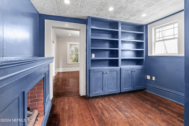 interior space with baseboards, dark wood-style floors, an ornate ceiling, built in shelves, and a fireplace