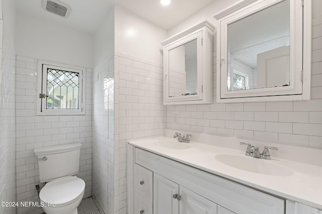 bathroom featuring toilet, tile walls, visible vents, and a sink