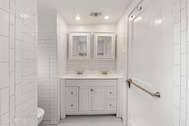 bathroom with double vanity, visible vents, tile walls, toilet, and a sink