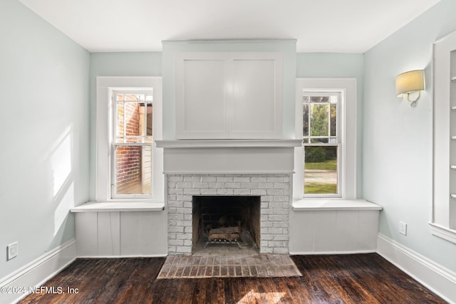 unfurnished living room featuring dark wood-style floors, a brick fireplace, and baseboards