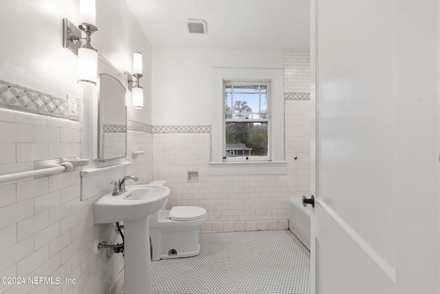 full bathroom featuring toilet, a wainscoted wall, tile patterned floors, tile walls, and a tub