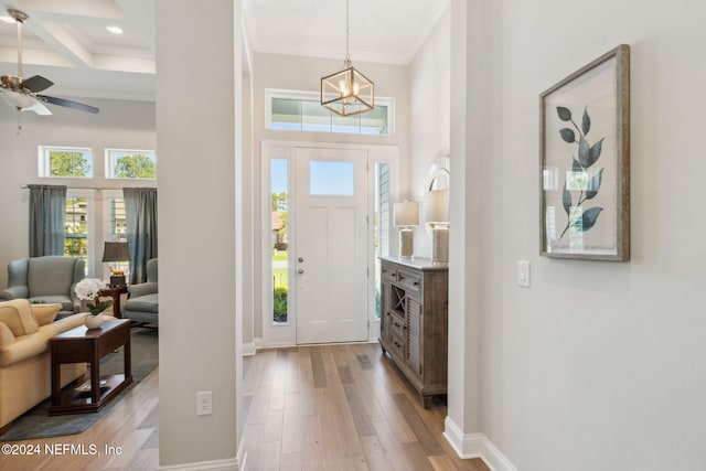 foyer with ceiling fan with notable chandelier, light wood-type flooring, a towering ceiling, and beam ceiling