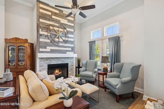 interior space featuring wood-type flooring, a stone fireplace, ornamental molding, and ceiling fan