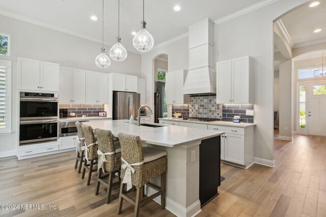 kitchen with appliances with stainless steel finishes, white cabinetry, light wood-type flooring, a kitchen island with sink, and sink