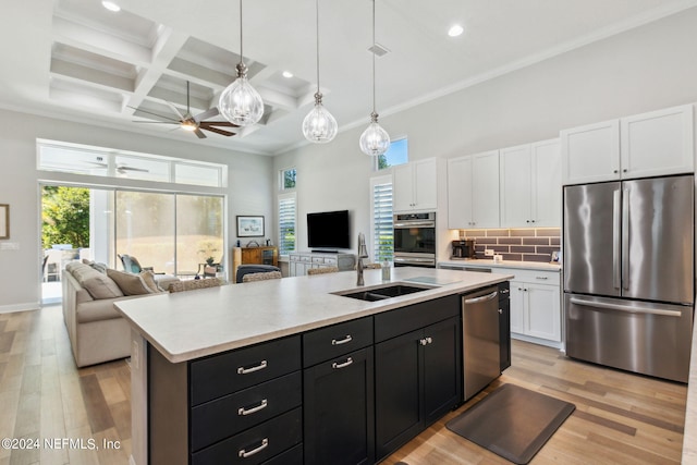 kitchen with appliances with stainless steel finishes, coffered ceiling, white cabinetry, light wood-type flooring, and a kitchen island with sink