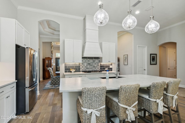 kitchen featuring light wood-type flooring, stainless steel fridge, a center island with sink, and white cabinets