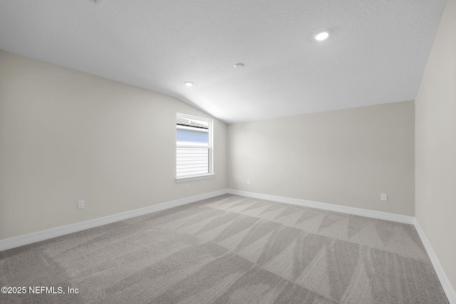 spare room featuring a textured ceiling, light carpet, and lofted ceiling