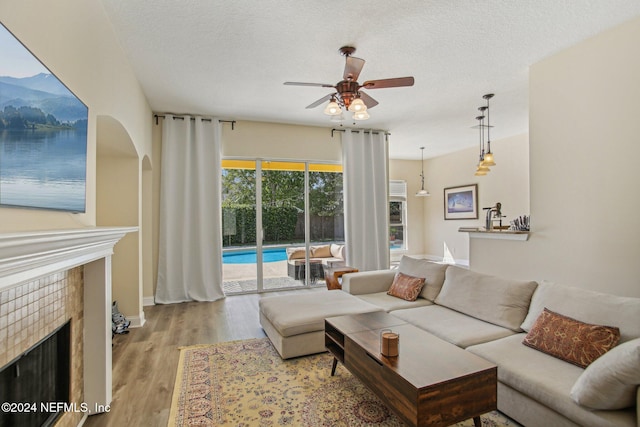 living room with light hardwood / wood-style flooring, a textured ceiling, a fireplace, and ceiling fan