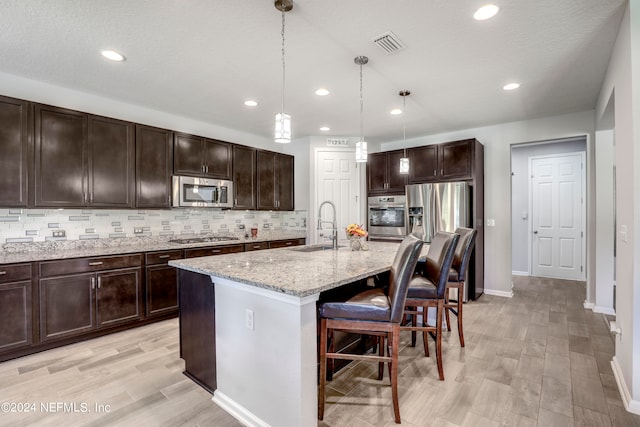 kitchen with a breakfast bar area, an island with sink, dark brown cabinets, pendant lighting, and appliances with stainless steel finishes