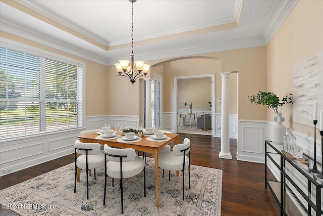 dining area with a raised ceiling, decorative columns, dark hardwood / wood-style flooring, crown molding, and an inviting chandelier