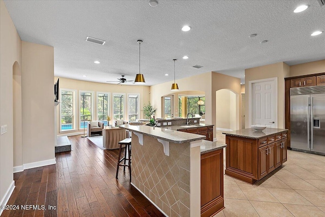 kitchen featuring a spacious island, built in fridge, a breakfast bar, pendant lighting, and light wood-type flooring