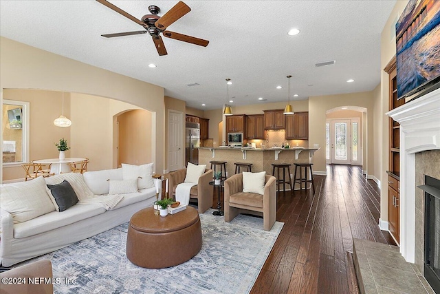 living room with a textured ceiling, ceiling fan, a fireplace, and dark hardwood / wood-style flooring