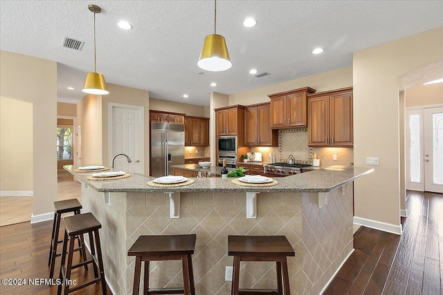 kitchen with dark wood-type flooring, built in appliances, a kitchen breakfast bar, and a textured ceiling