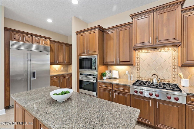 kitchen with a textured ceiling, tasteful backsplash, light stone counters, and built in appliances