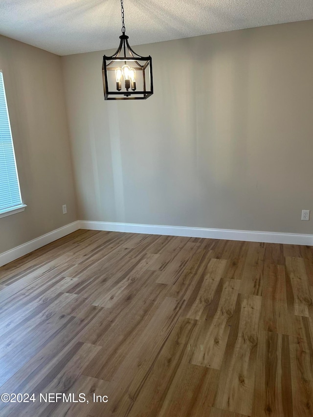 empty room featuring hardwood / wood-style floors, a textured ceiling, and a notable chandelier