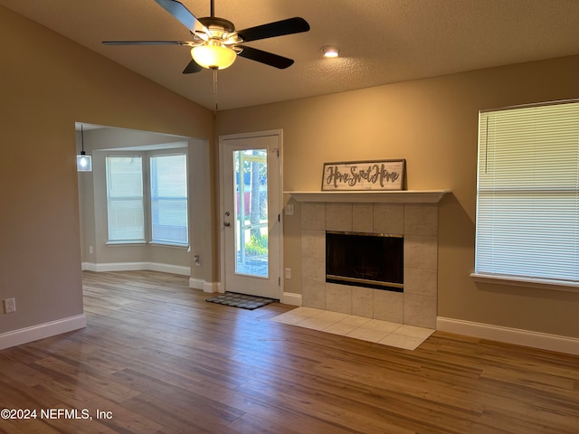 unfurnished living room with a textured ceiling, vaulted ceiling, ceiling fan, a tile fireplace, and hardwood / wood-style flooring