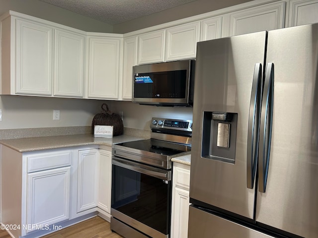 kitchen with white cabinetry, light hardwood / wood-style flooring, stainless steel appliances, and a textured ceiling