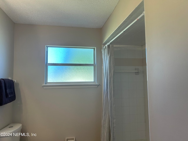 bathroom with a textured ceiling, toilet, and curtained shower