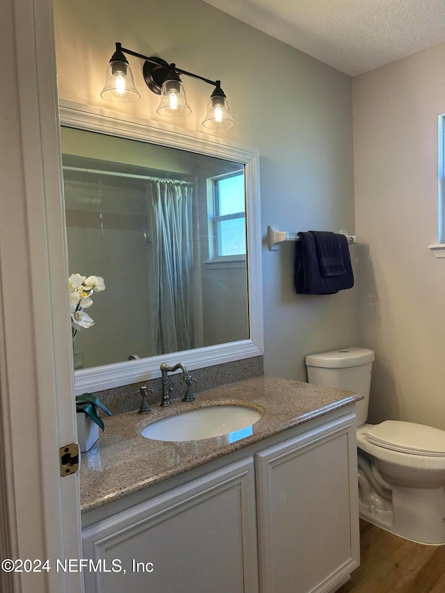 bathroom featuring a shower with shower curtain, vanity, a textured ceiling, hardwood / wood-style floors, and toilet