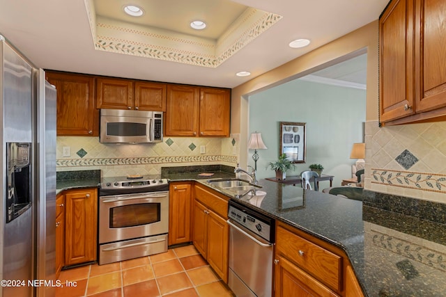 kitchen featuring appliances with stainless steel finishes, kitchen peninsula, a tray ceiling, and dark stone counters