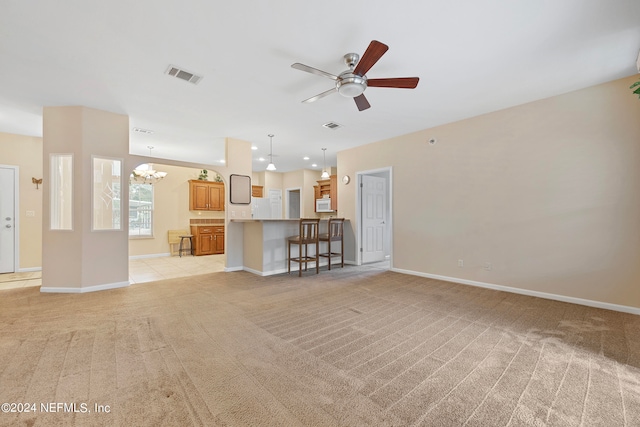 unfurnished living room featuring ceiling fan with notable chandelier and light colored carpet