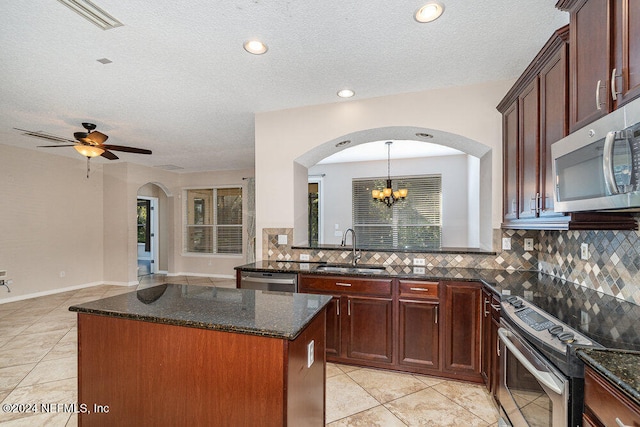 kitchen featuring a center island, ceiling fan with notable chandelier, dark stone counters, appliances with stainless steel finishes, and sink