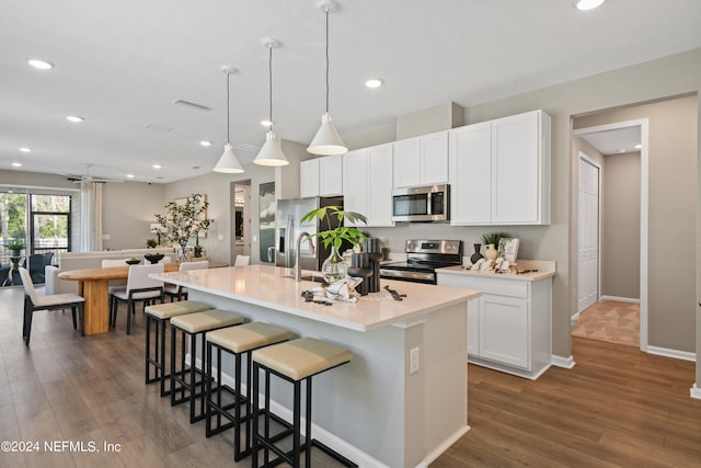 kitchen with a kitchen island with sink, decorative light fixtures, stainless steel appliances, and dark hardwood / wood-style flooring