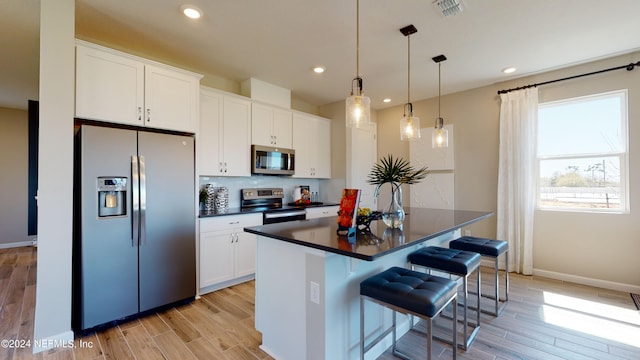 kitchen featuring stainless steel appliances, a kitchen bar, light wood-type flooring, and white cabinetry