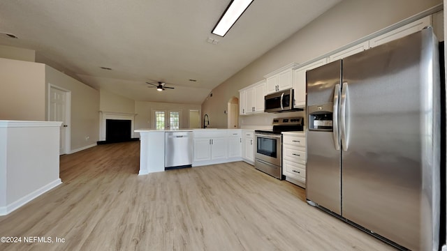 kitchen featuring light wood finished floors, a peninsula, a sink, appliances with stainless steel finishes, and open floor plan