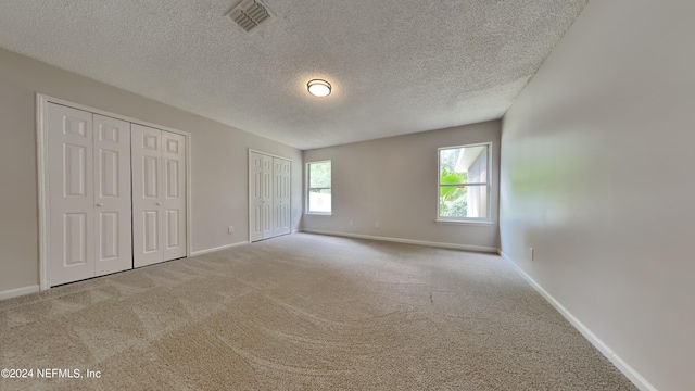 unfurnished bedroom featuring a textured ceiling, multiple closets, and light colored carpet