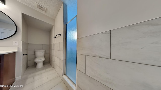 bathroom with vanity, a walk in shower, a textured ceiling, tile walls, and toilet